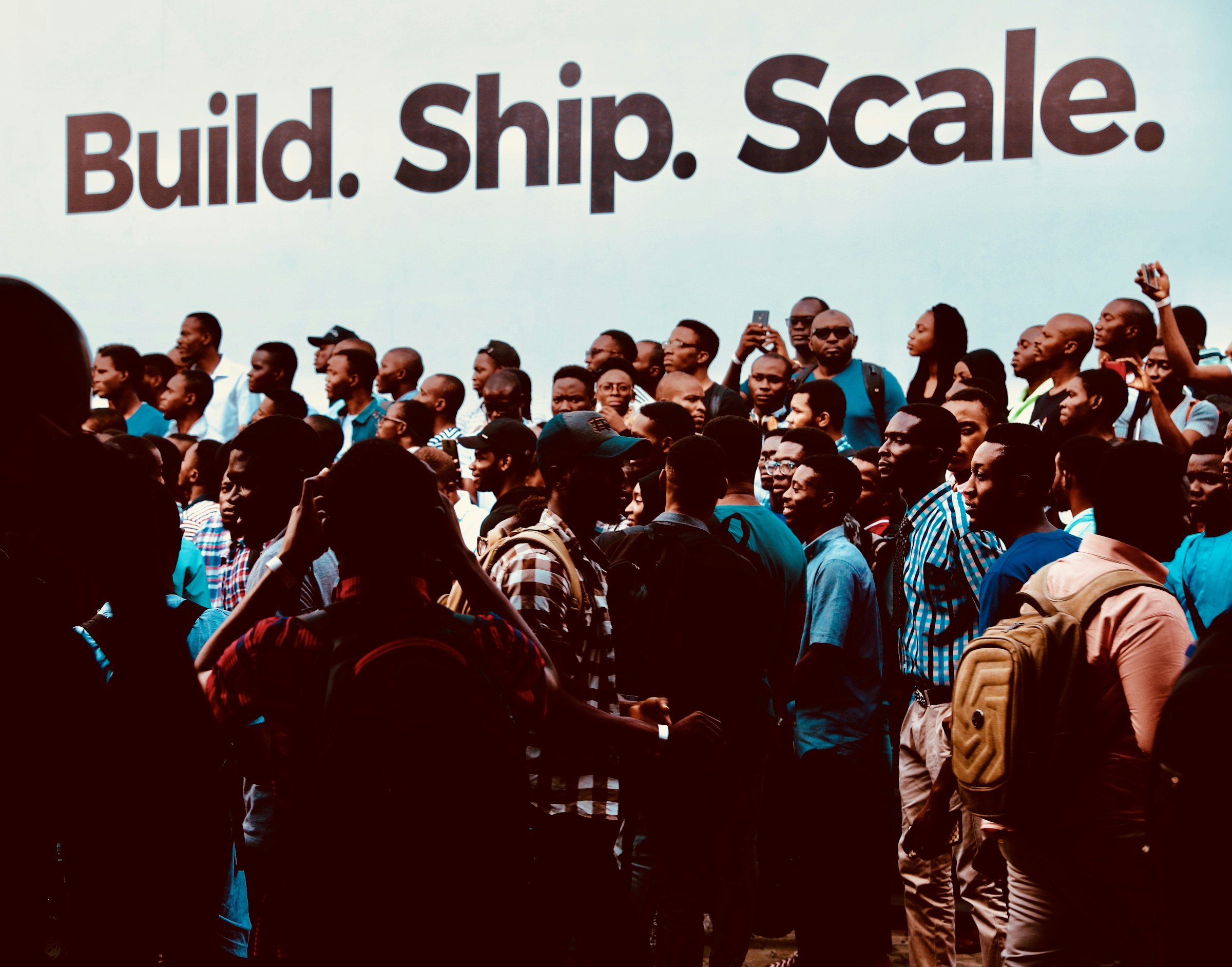 A large crowd of developers and builders gathered beneath a “Build. Ship. Scale.” banner